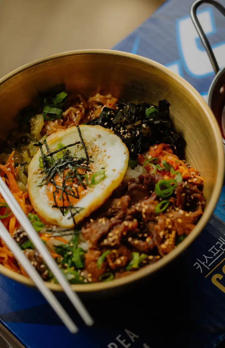Bibimbap w złotej misce z jajkiem sadzonym, nori i warzywami, obok pałeczki