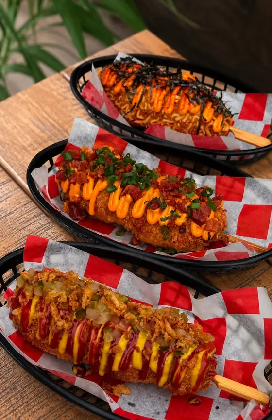 Trzy corn dogi z sosami w koszykach na papierze w czerwoną kratę