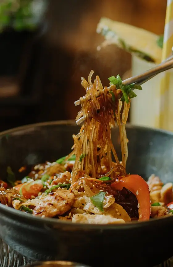 Japchae z kurczakiem i papryką, makaron podniesiony pałeczkami nad miską