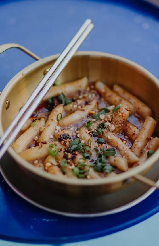 Tteokbokki z olejem chili, dymką i chrupiącą posypką w złotym garnku z pałeczkami